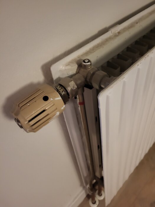 Radiator med termostat och röranslutning i ett rum, där ett litet kvadratiskt vred syns på toppen.