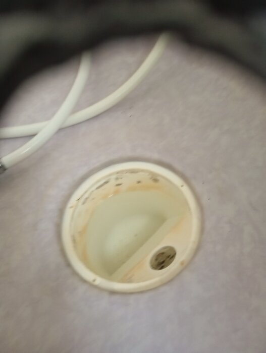 Golvbrunn med närbild på insats, omgiven av vitt golv och vita rör i bakgrunden. Fråga om vilken vattenlåsinsats som passar.