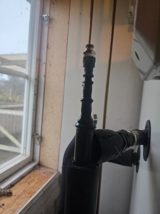 Ventil eller rördel vid ett fönster, delvis täckt av isolering.