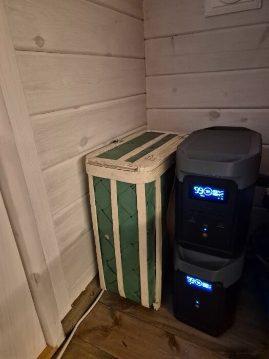 Powerstation och extra batteri i ett hörn av ett rum med träpanel.