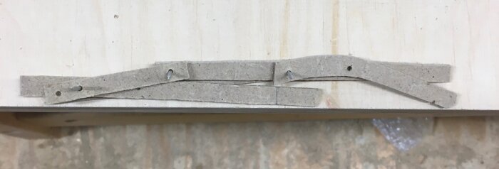 Mockup av hopfällbar stol med kartongbitar på en träyta, designad för ställbar lutning och sittshöjd. Planeras för flätad sits och rygg.