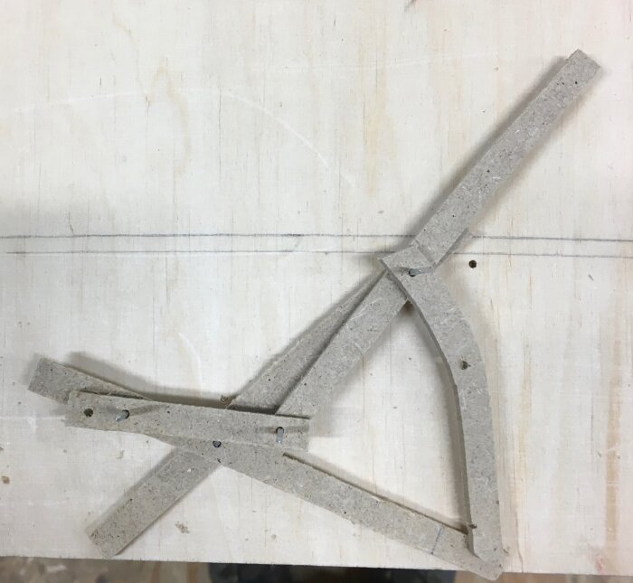 Mockup av en ställbar och hopfällbar stol i kartong, visar en enkel saxdesign med justerbar lutning och höjd, på en träyta.