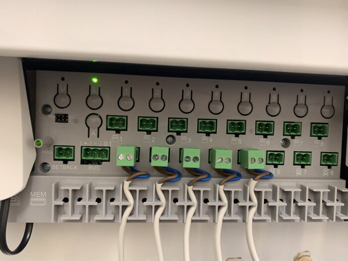 Elektrisk kopplingsdosa med gröna terminaler och kablar; en grön LED-lampa vid "L"-knappen lyser. Ingen nätverkskoppling syns.