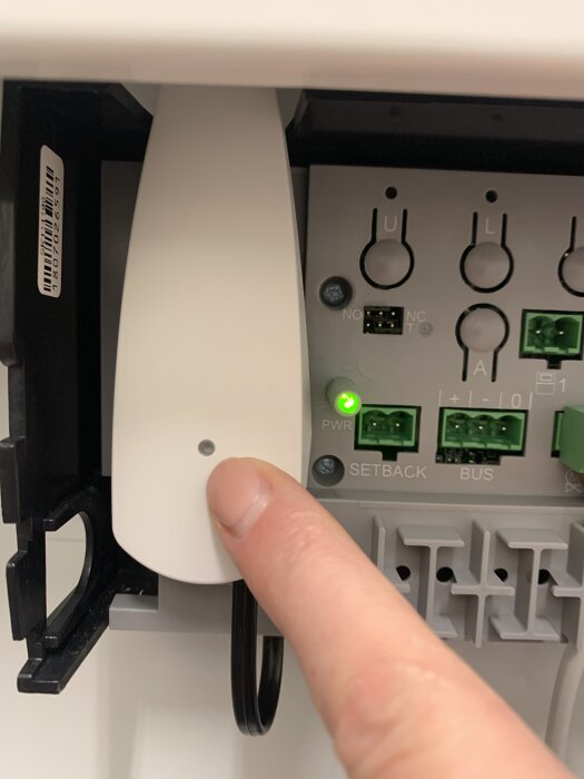 Person pekar på golvvärmekontrollpanel med knappar och LED-lampor, varav en lampa lyser grönt.