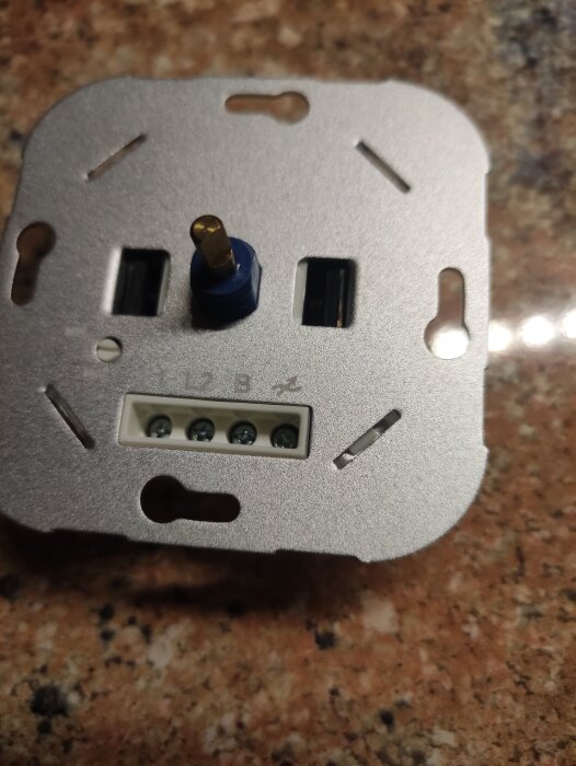 Baksidevy av en dimmer med skruvkopplingar och anslutningar, placerad på en fläckig stenyta.