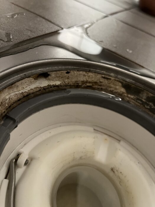 Golvbrunn i badrum med synlig kant utan fogmassa och vatten på kaklet.