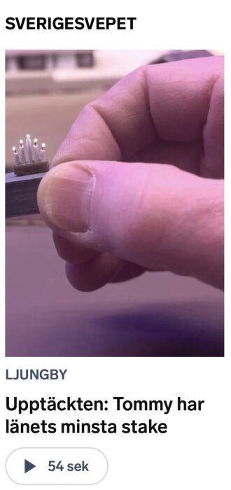 En hand håller ett litet föremål med flera små lysdioder eller nålar fastsatta på en platta. Bakgrunden är suddig.