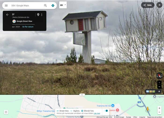 Ett fågelhusformat torn på en äng, med en vägskylt och molnig himmel i bakgrunden.