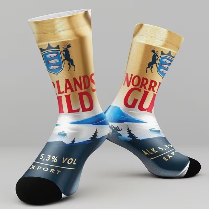 Strumpor med design av ett ölburksmärke, med älg och landskap, i guld och blå färg. Text och symboler ingår i mönstret.