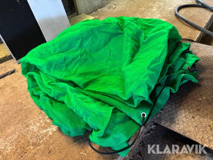 Grönt finmaskigt lastnät på marken, används för att dämpa damm när man suger upp löv i en kärra.