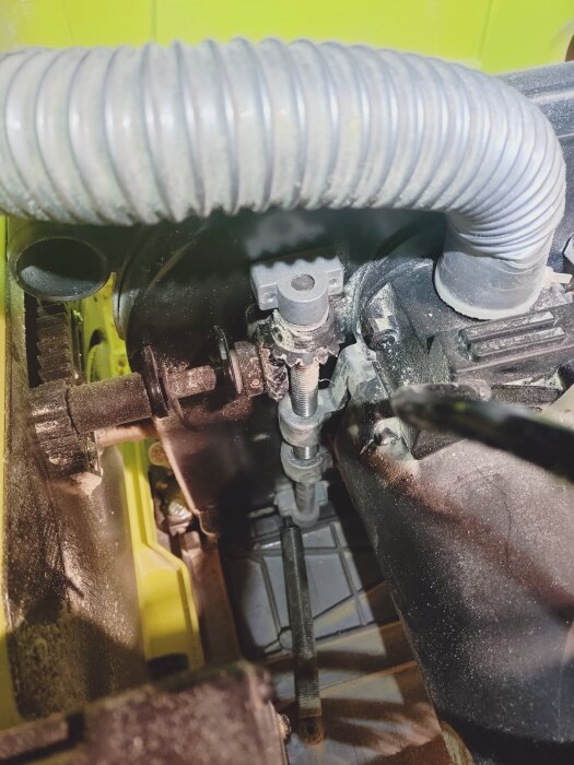 Närbild av bordssågens inre mekanism där damm och spån har fastnat i gängorna nära styrstången och grå slang löper ovanför.