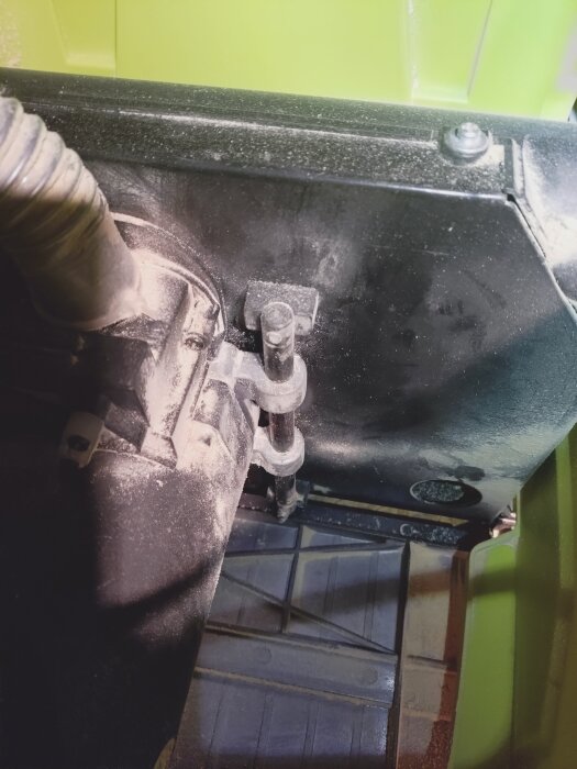 Närbild på mekanismen under en bordssåg; spån synliga kring gängor där höjdfunktionen låser sig.