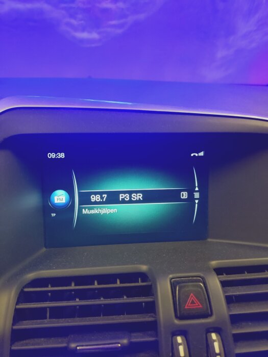 Bilradio som visar P3 SR och Musikhjälpen, fotograferad inne i bilen med blått ljus från omgivningen. Klockan visar 09:38.