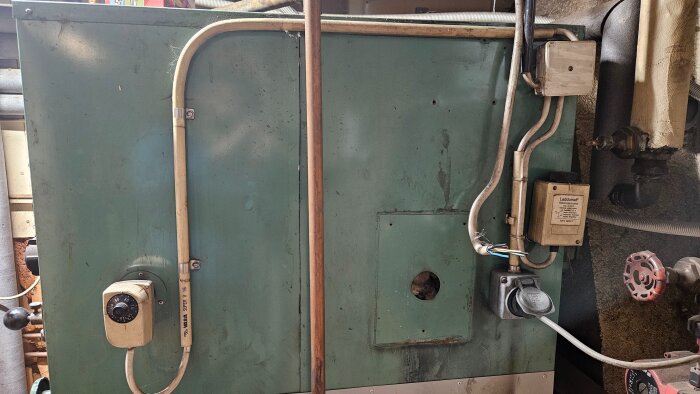 Bild av en laddomat med två rattar, den vänstra visar 85, och flera röranslutningar. Märkt med "Laddomat rökrörstermostat".