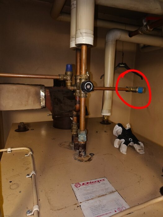 Kopparrör med ventil och blått handtag, omgivet av andra rör under diskbänk. Röd cirkel markerar delen av röret med ventilen.