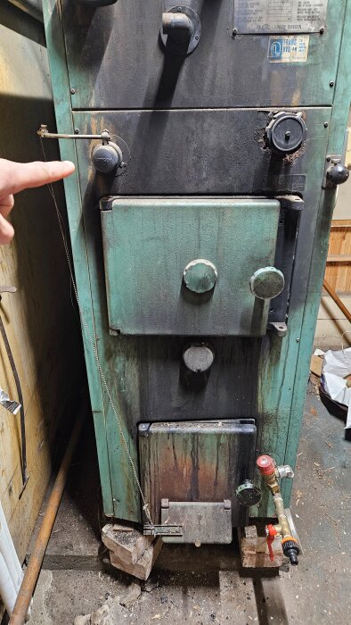 Panna med grön lucka och ett kedjesystem som reglerar öppningen, samt en person som pekar på en komponent vid pannan.