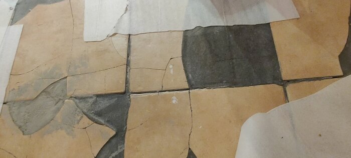 Skadade klinkerplattor med sprickor och fyllningar av flytspackel ovanpå ett undergolv.