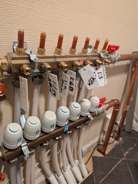 Lk Systems golvvärmesystem med flera slangar, ställdon och märklappar, två ställdon verkar stängda enligt texten ovan.