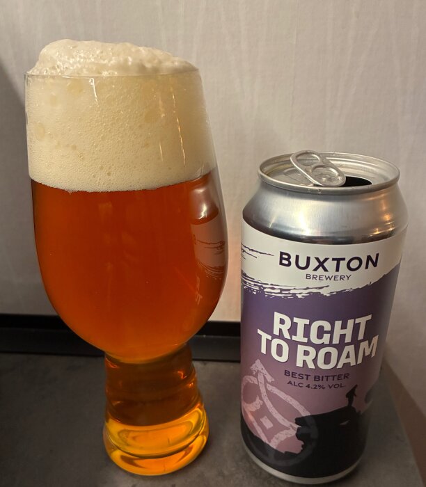 Ett glas öl med tjock skumkrona bredvid en öppnad burk med etikett "Buxton Brewery Right to Roam Best Bitter".