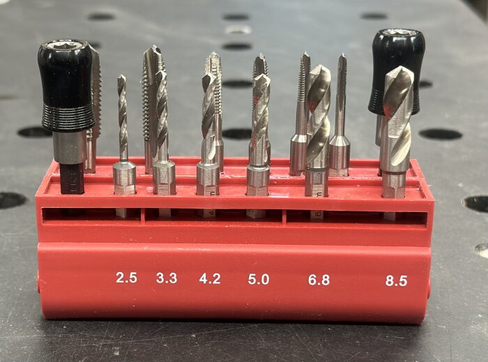 En röd verktygshållare med åtta olika borr och gängverktyg, märkt med storlekarna 2.5 till 8.5.
