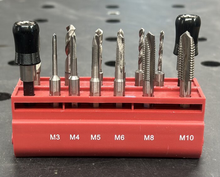 Verktygssats i röd hållare med borr och gängverktyg märkta M3 till M10, placerade på ett svart underlag.