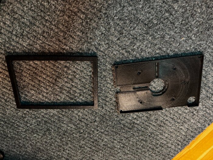 Svart plastkåpa och rektangulär ram på ett grått mattunderlag, relaterat till ett byggprojekt med kabelinstallation.