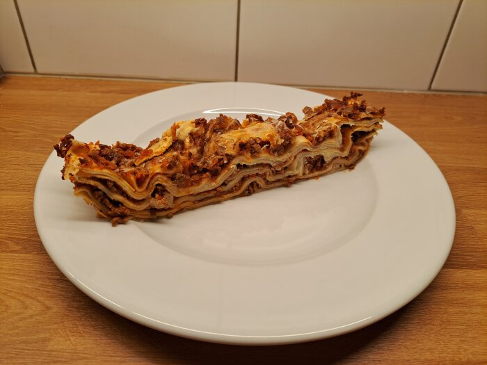 En lasagnebit med flera lager av pasta och köttfärssås på en vit tallrik.