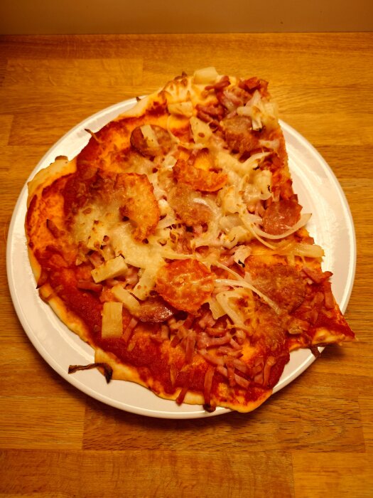 Hemgjord pizza på en tallrik med tomatsås, skinka, ost, ananas och lök, serverad på ett träbord.