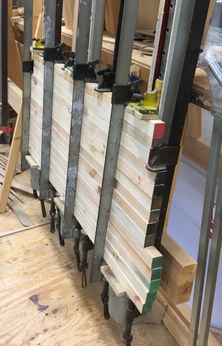 Granstavar limmade ihop och fastklämda i tvingar på en arbetsbänk, används som distansmaterial för byggprojekt.