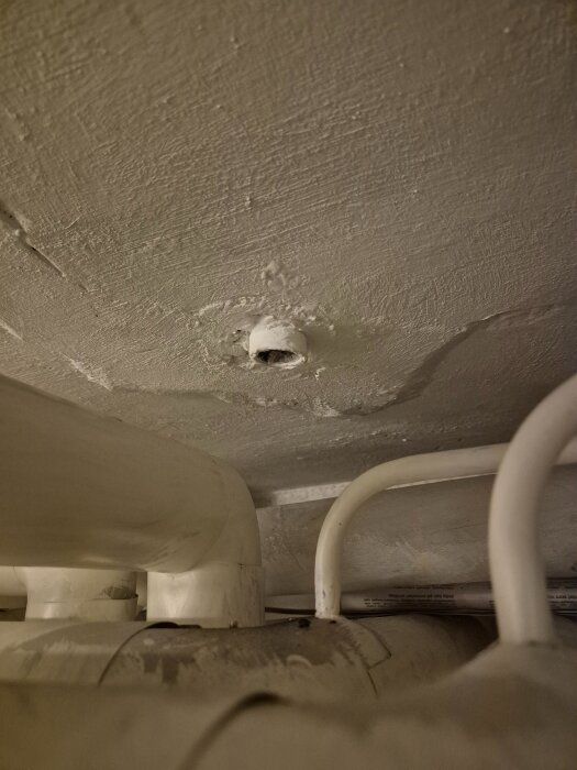 Närbild av en vitmålad rörstump som sticker ut från ett tak med flera böjda rördelar runtom.