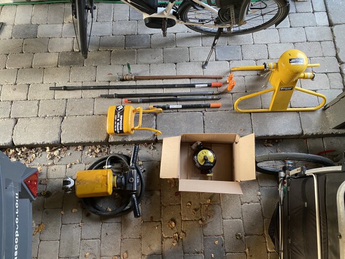 Verktyg och utrustning för bergborrning arrangerade på stenlagd yta. Inkluderar borrstänger, borrkrona och kompressor.