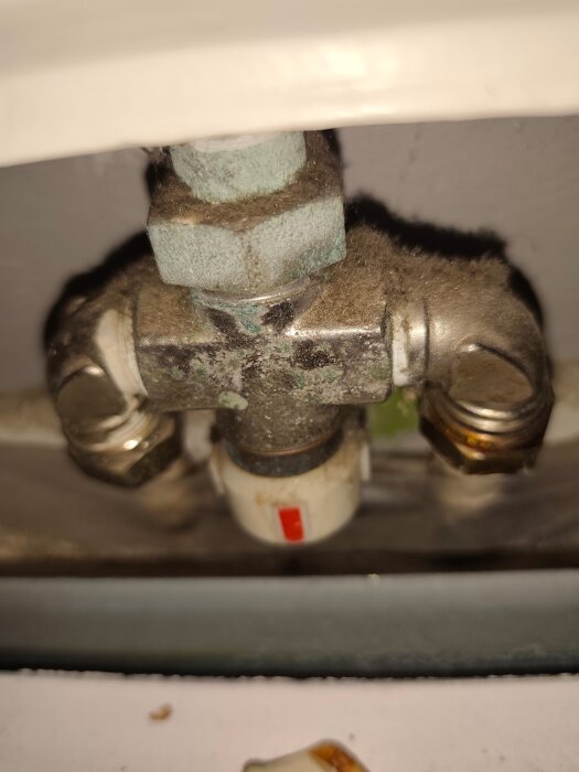 Närbild av ett termostatvred med ett rött märke, fastsatt vid en smutsig rörledningsanslutning.