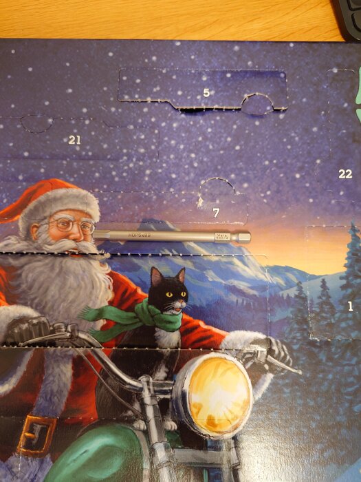 Julkalender med tomte och svartvit katt på motorcykel mot snöig bergsbakgrund, dolda luckor med nummer.