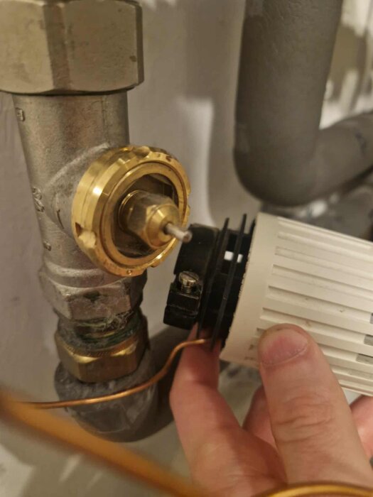 Termostat nedanför shuntventilen med en hand som justerar inställningen.