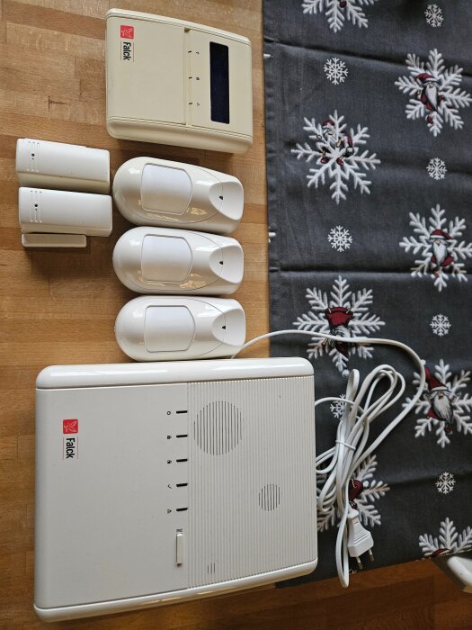 Alarmutrustning på ett bord: gulnad manöverpanel, larmcentral, tre rörelsedetektorer, och två magnetkontakter.