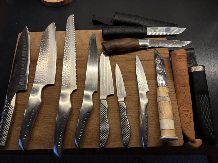 En uppsättning av åtta olika köksknivar och två knivar med fodral placerade på en skärbräda.