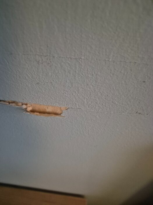 Skadad vägg med löst sittande tapet och färg, visar underliggande yta i sovrummet under renovering.