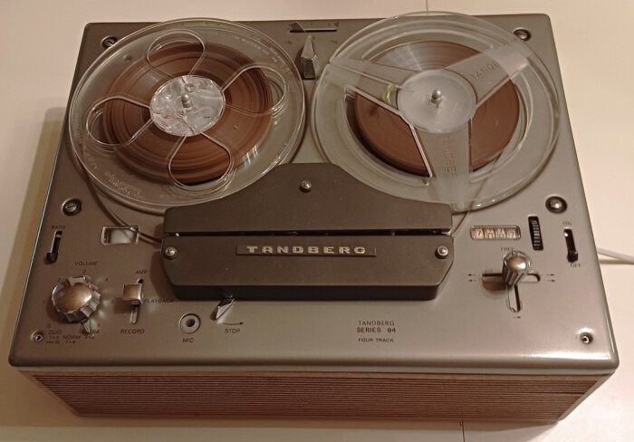 Tandberg rullbandspelare från 1965 med två spolar, volym- och basskontroller samt märket Tandberg på framsidan.