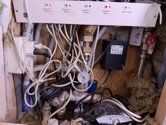 Golvvärmesystem med rör, ventiler och elektronik i ett underhållsutrymme, kablar och isolering runt om.