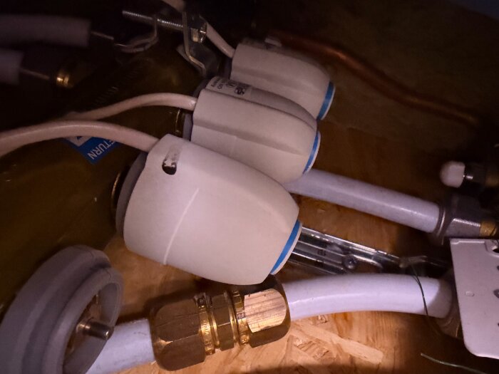 Golvvärmesystem med tre vita termostater och kopparrör synliga i en byggnadsmiljö.