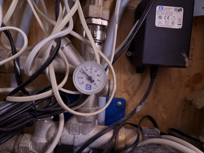 Närbild av rörsystem med termometer och kablar, del av golvvärmesystem med fokus på möjliga underhållsbehov som luftning och service.