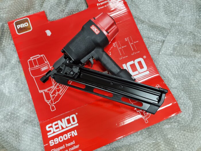 Pneumatisk spikpistol Senco S900FN på röd förpackning med skyddsplast i bakgrunden.