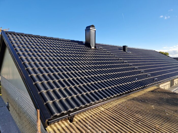 Nytt svart tak med tegelpannor, blå himmel och skorsten i fokus.