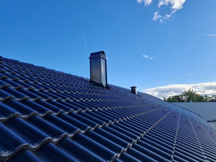 Tak med mörka takpannor och två skorstenar mot en klarblå himmel.