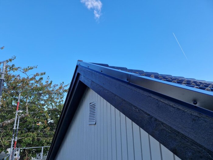 Ett nylagt tak fotograferat från sidan mot en klarblå himmel med en vit kondensstrimma och träd i bakgrunden.