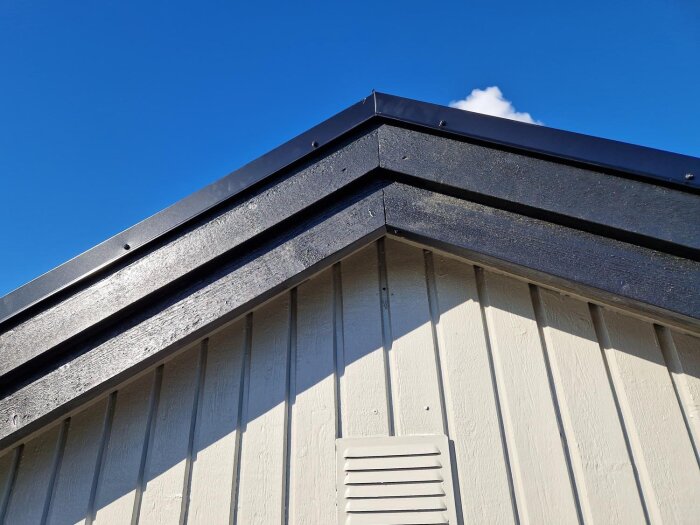 Taket på ett hus med svarta takplattor och en blå himmel i bakgrunden.