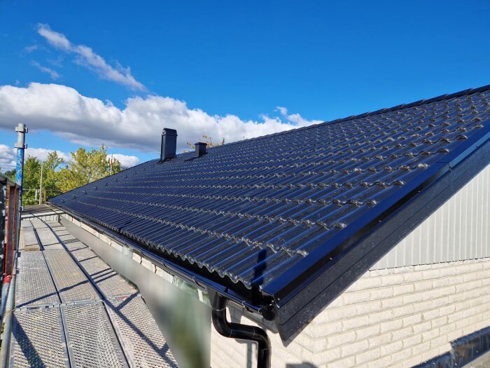 Nylagt svart tak med tegelprofil under klarblå himmel. Scen från byggarbetsplats med ställning runt taket.