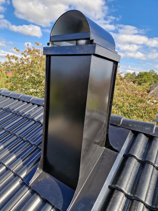 Ett nylagt svart tak med en skorsten under klarblå himmel.