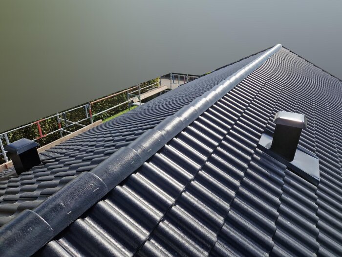 Svart tak med tegelprofiler och två takventilationer, fotograferat i solljus.