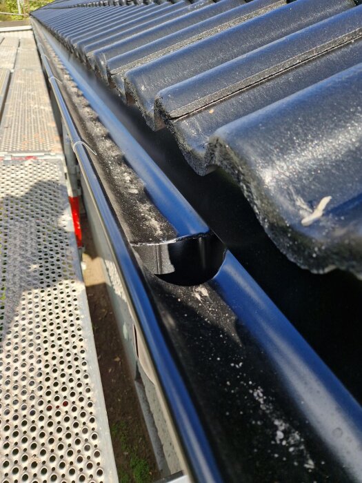 Svart tak med takpannor fotograferat nära. Del av takränna syns, med byggnadsställning bredvid. Feel free to ask if you need anything else!